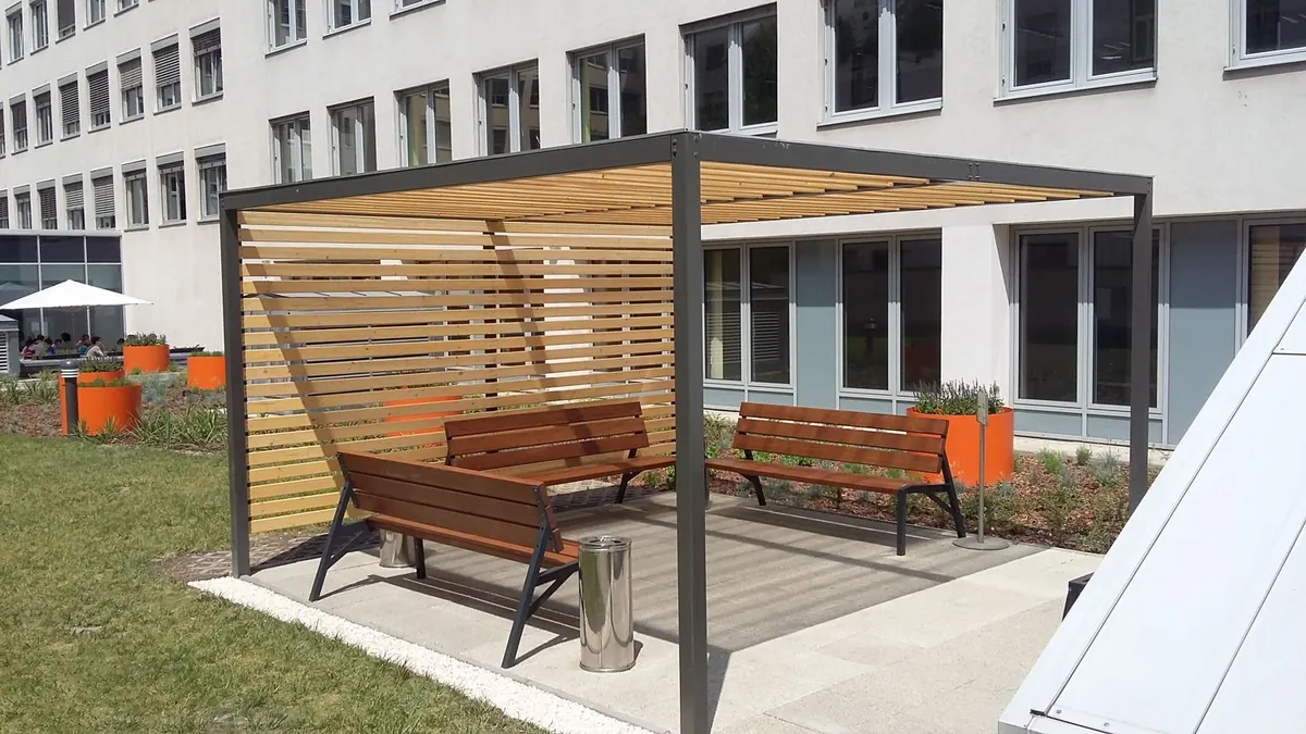 Acélvázas pergola fa lécekkel és padokkal egy irodaház udvarán